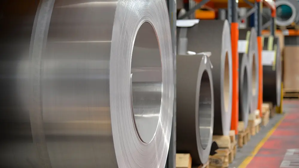Aluminiumrollen (Coils) gelagert auf Holzpaletten, im Vordergrund steht eine naturblanke Alurolle, dahinter findet man weitere Bänder und Bleche aus Aluminium.