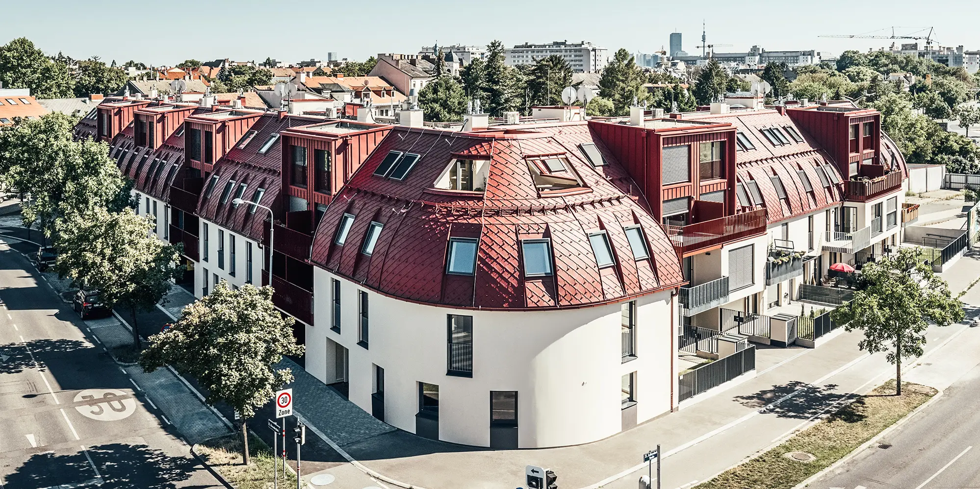 Widok ulicy na osiedle mieszkaniowe Schöneck 13 i zaokrąglony krajobraz dachów, zaprojektowany przez biuro architektoniczne schneider+schumacher.