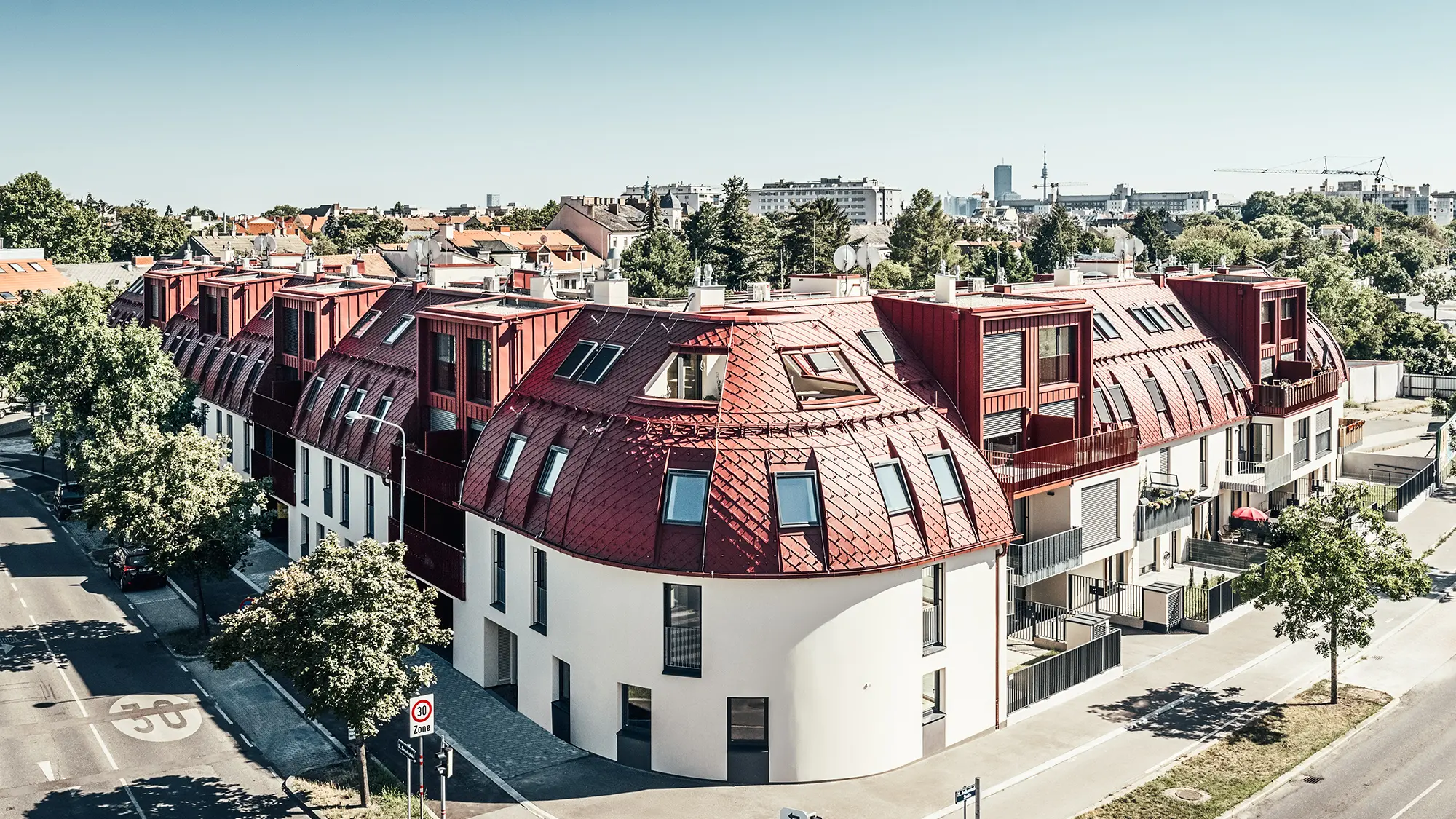 Widok ulicy na osiedle mieszkaniowe Schöneck 13 i zaokrąglony krajobraz dachów, zaprojektowany przez biuro architektoniczne schneider+schumacher.