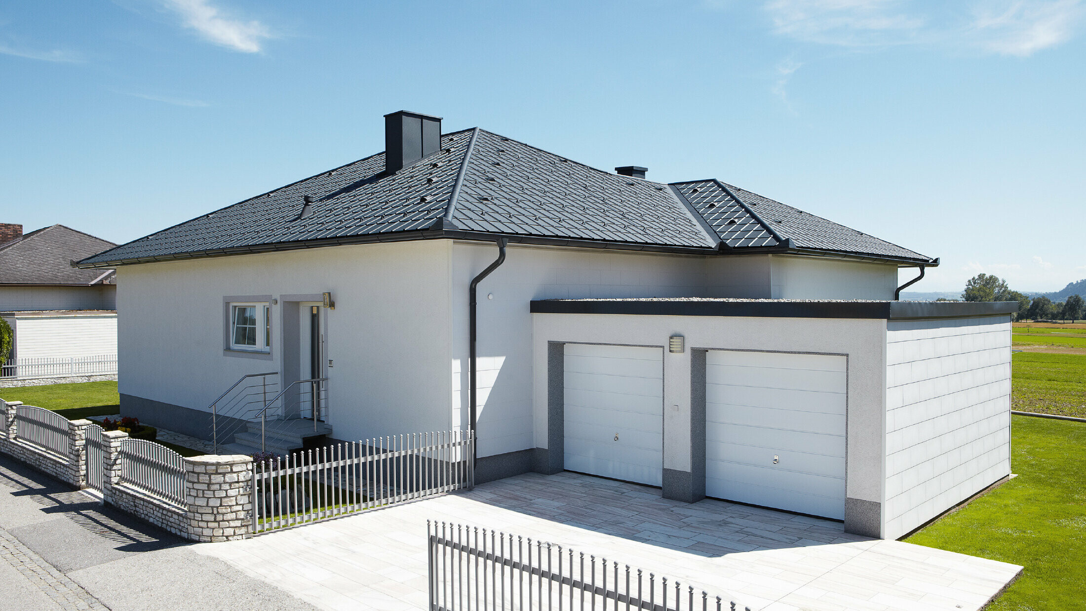 Der neugebaute Bungalow mit Zeltdach wurde mit der PREFA Dachplatte in P.10 Anthrazit eingedeckt. Rechts daneben wurde eine Doppelgarage angebaut, fotografiert wurde von der Straße aus.