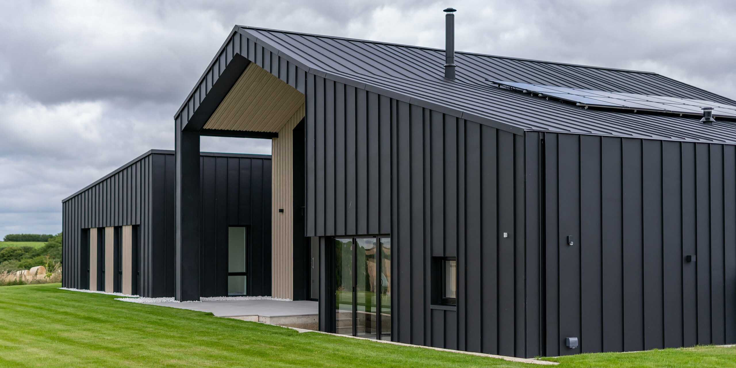 Schrägansicht der Rückseite von ‚The Hide‘ in Cornwall mit PREFALZ Dach- und Fassadenbekleidung in P.10 Anthrazit. Die klare Stehfalzoptik des Daches und der Fassade aus Aluminium erzeugt eine moderne und harmonische Linienführung, die durch Holzelemente und die umgebende Natur ergänzt wird -ein perfektes Zusammenspiel von Funktionalität und Ästhetik.