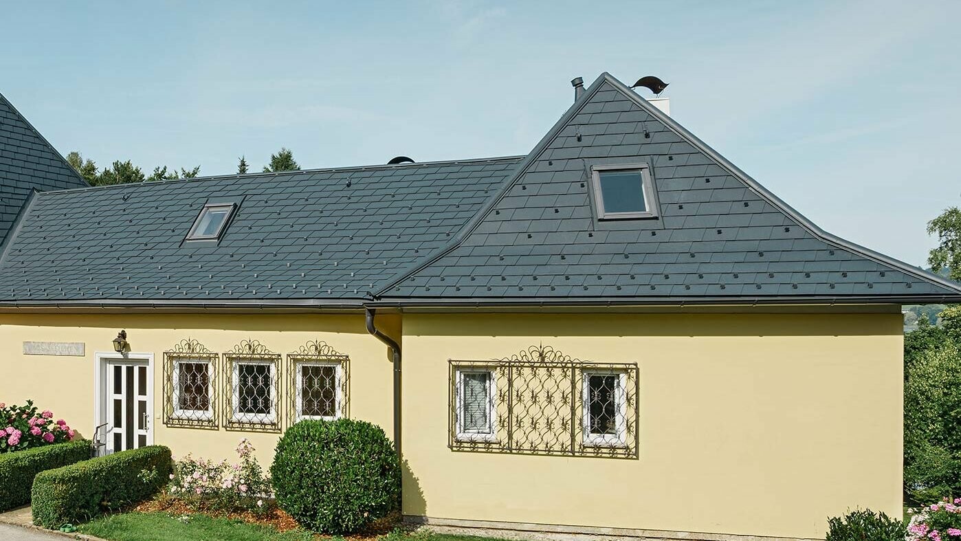 Einfamilienhaus mit Walmdach und mit gelber Putzfassade; Das Dach wurde mit der PREFA Dachschindel in Anthrazit eingedeckt.