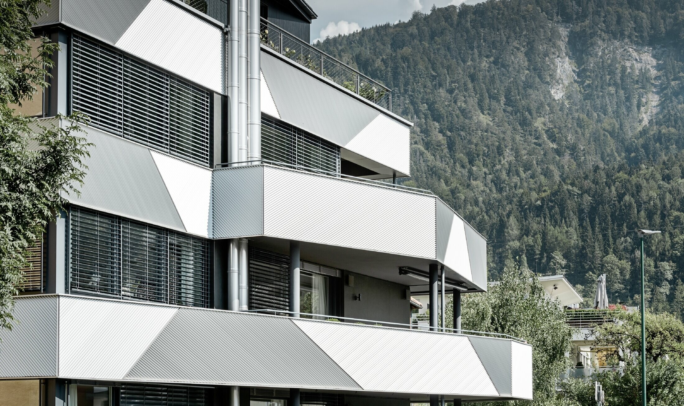 Aranżacja elewacji domu wielorodzinnego z balkonami i lodżiami z profilem trójkątnym PREFA położonym ukośnie.