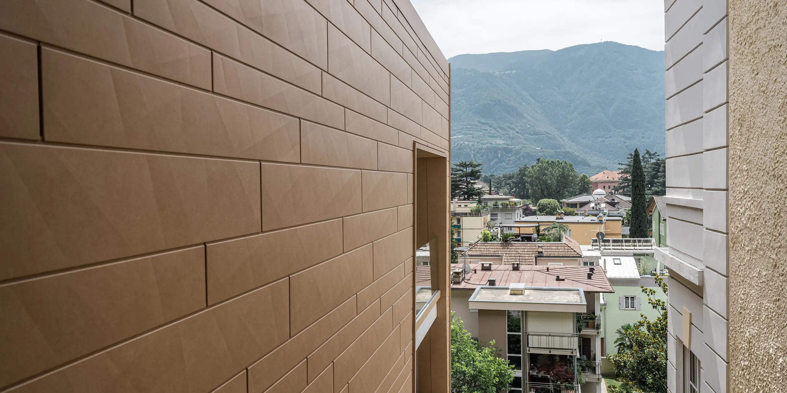 Detailaufnahme der modernen PREFA Siding.X Fassade in P.10 Sandbraun an der Villa Laura in Bozen, Italien. Die harmonisch gefügten Aluminiumelemente bieten eine langlebige und ästhetische Lösung, die sich anmutig in die malerische Bergkulisse Südtirols einfügt. Die Fassade spiegelt die Innovation und Qualität wider, für die PREFA Aluminiumprodukte bekannt sind. Zudem setzt die Gebäudehülle aus Aluminium einen warmen Farbakzent in der urbanen Landschaft.