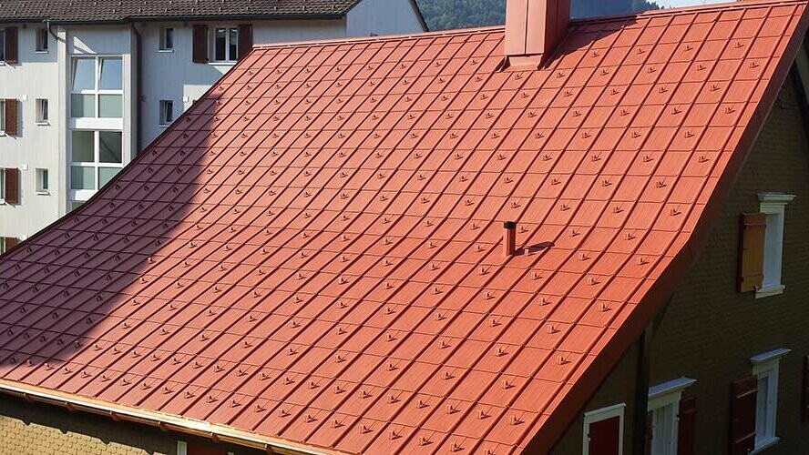 Dach dwuspadowy pokryty dachówką klasyczną PREFA z aluminium. Dach w kolorze ceglastym z barierami śniegowymi i kominem