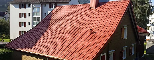 Dach dwuspadowy pokryty dachówką klasyczną PREFA z aluminium. Dach w kolorze ceglastym z barierami śniegowymi i kominem