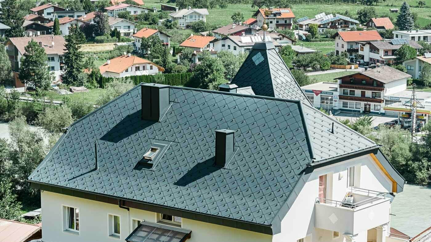 Klasyczny dach szczytowy z dwoma oknami dachowymi i wieloma dodatkowymi oknami, kryty dachówką rombową PREFA 44 x 44 w kolorze jasnoszarym.