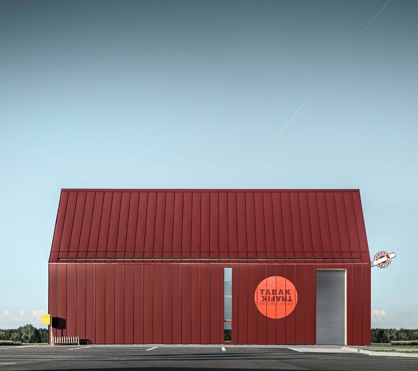 Nowoczesny sklep tytoniowy z dachem dwuspadowym bez okapu, z okładziną aluminiową PREFA wykonaną w systemie pionowych i kątowych zakładek w kolorze specjalnym czerwono-czarnym