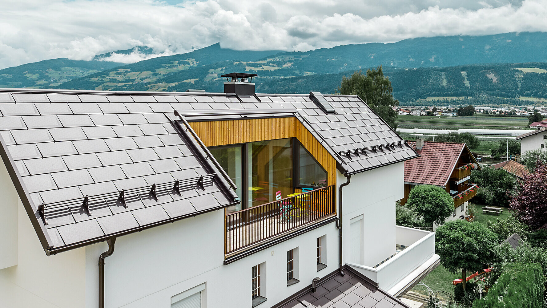 Dom mieszkalny pokryty aluminiową dachówką R.16 PREFA. Idealnie komponują się z dużym balkonem w kolorze orzechowym oraz tynkową elewacją. 
