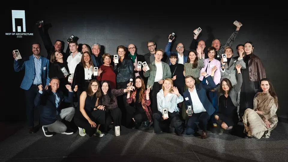 Zdjęcie grupowe zwycięzców podczas ceremonii wręczenia nagród „Budynek mieszkalny roku 2025”: zwycięzcy stoją przed elegancką czarną sceną z logo „Best of Architecture” i dumnie trzymają w rękach swoje nagrody. Dynamiczne pozy, nowoczesne ubrania i efektowne oświetlenie podkreślają znaczenie wydarzenia, a scena symbolizuje innowacyjność i doskonałość architektoniczną.