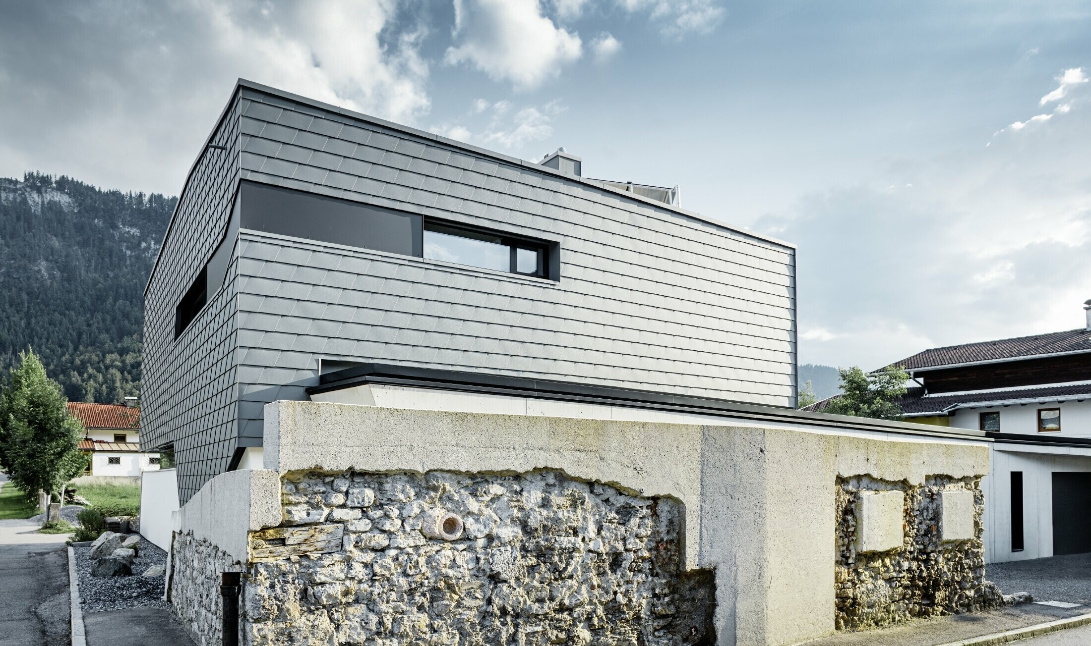 Nowoczesny dom jednorodzinny z płaskim dachem, dużymi powierzchniami okiennymi i aluminiowym łupkiem fasadowym PREFA w kolorze jasnoszarym