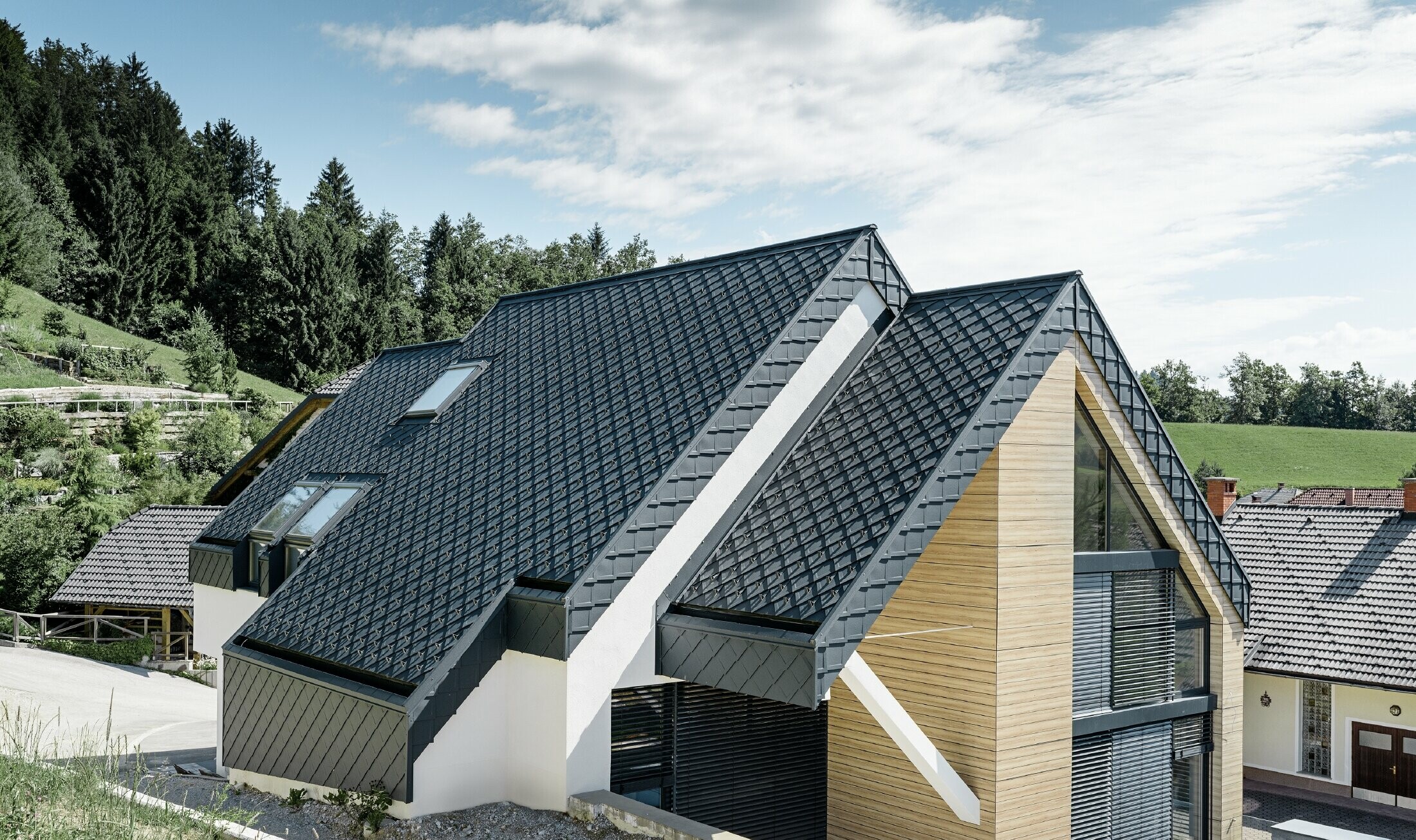 Dom jednorodzinny z dachem dwuspadowym bez występu dachowego, z elewacją o wyglądzie drewna i dachem aluminiowym w kolorze antracytowym