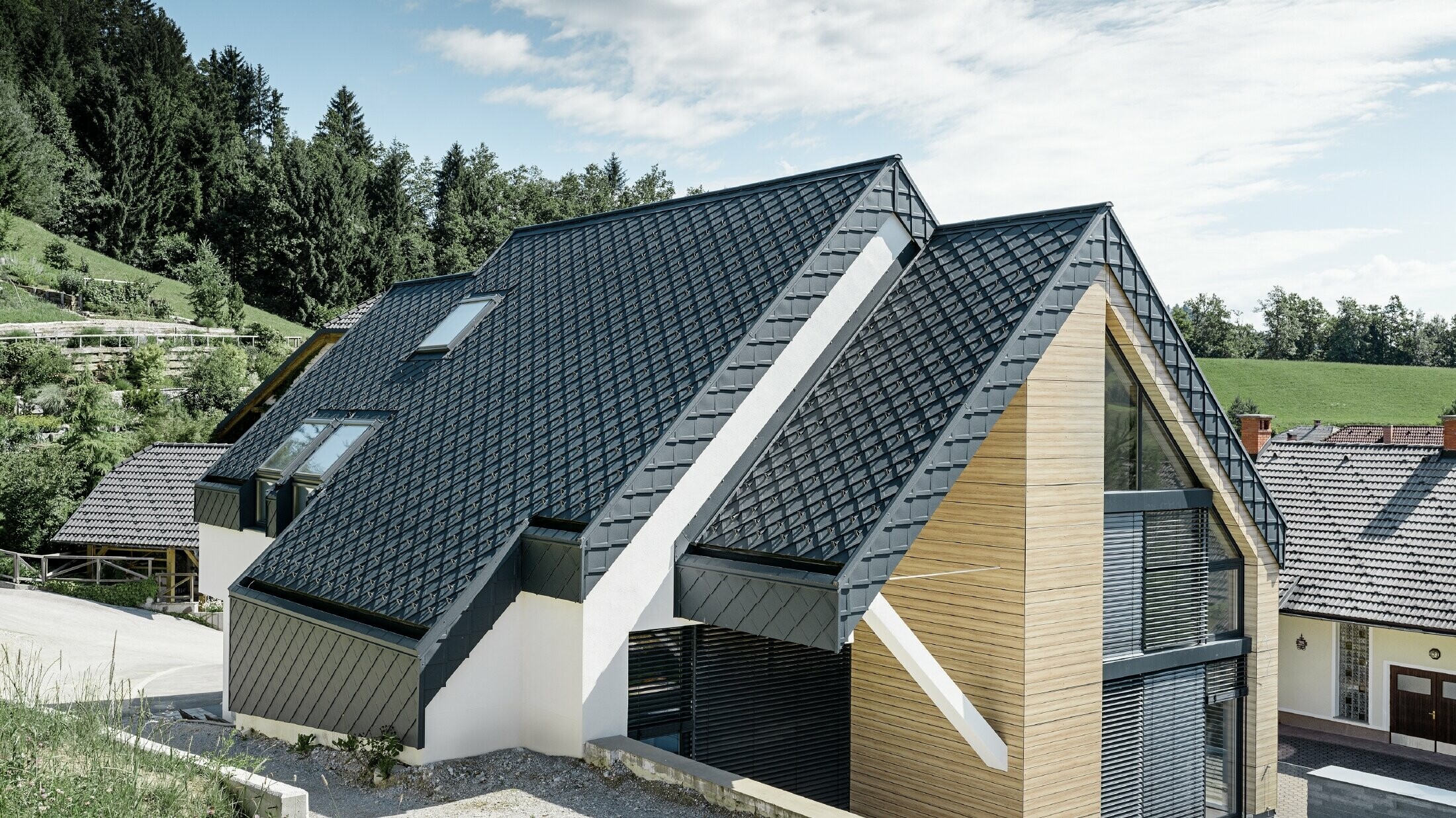 Dom jednorodzinny z dachem dwuspadowym bez występu dachowego, z elewacją o wyglądzie drewna i dachem aluminiowym w kolorze antracytowym
