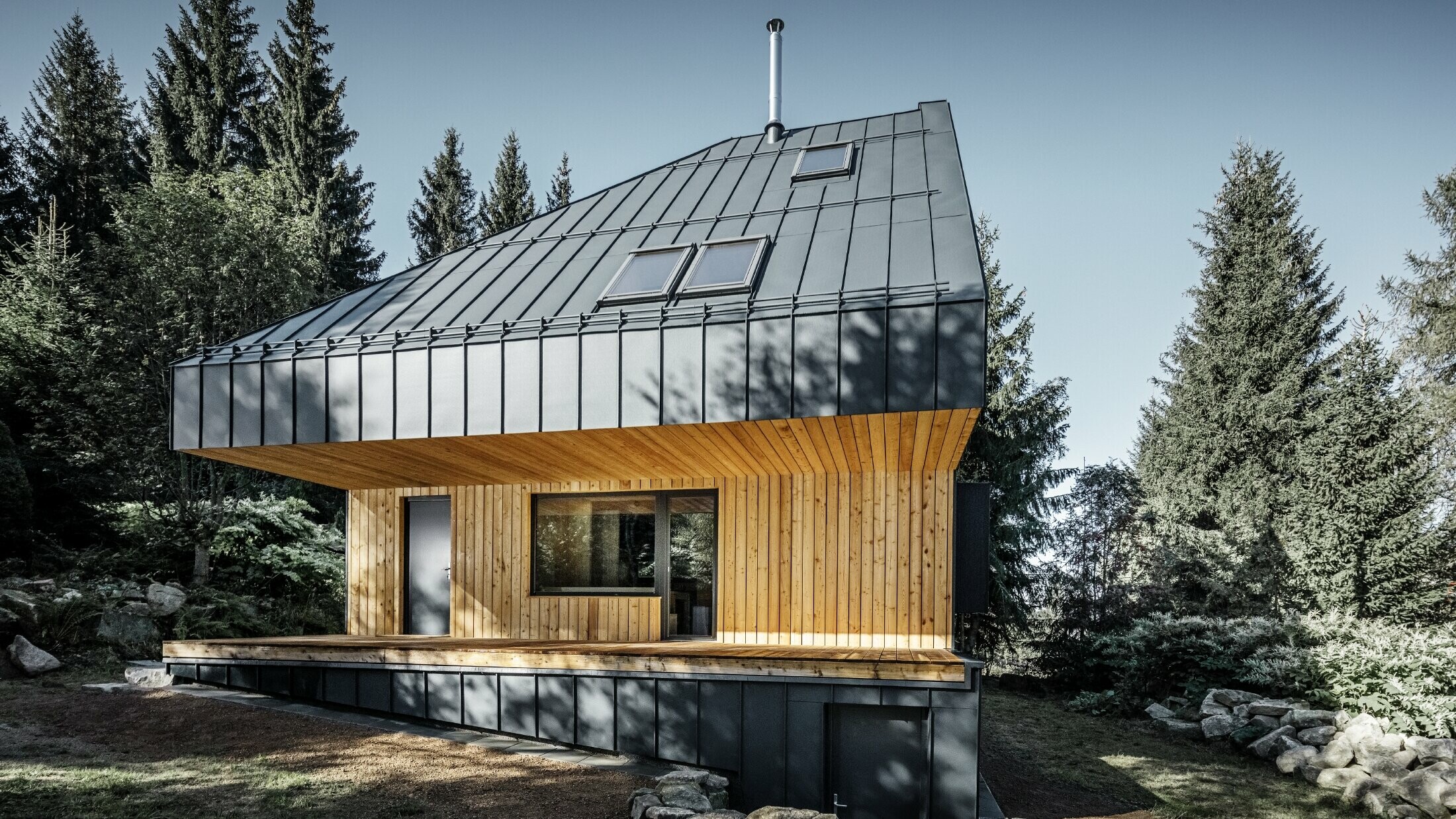 Architektoniczny dom jednorodzinny w lesie, imponujący dach został pokryty aluminium PREFA Prefalz w kolorze antracytowym. Podsufitka i elewacja są pokryte drewnianymi panelami.