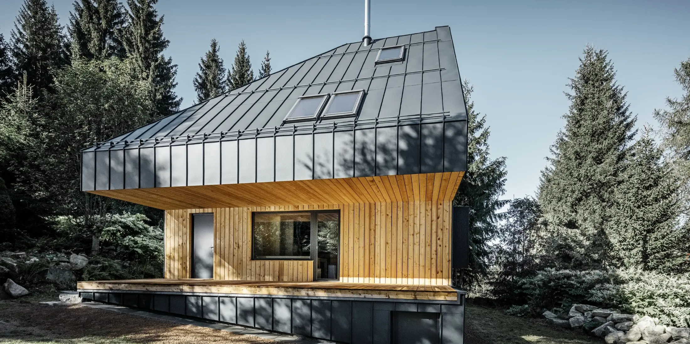 Architektoniczny dom jednorodzinny w lesie, imponujący dach został pokryty aluminium PREFA Prefalz w kolorze antracytowym. Podsufitka i elewacja są pokryte drewnianymi panelami.