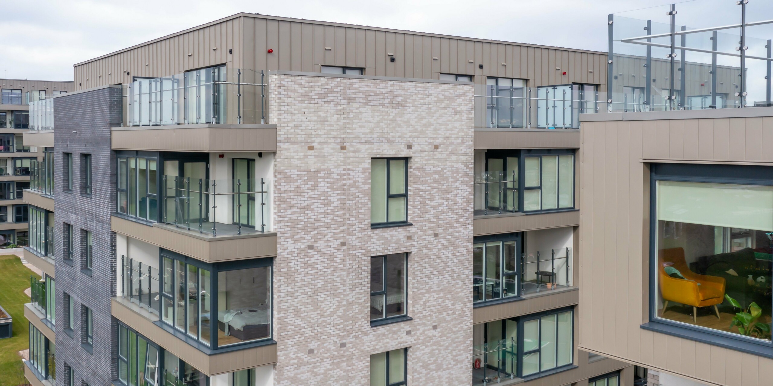 Drohnenaufnahme von Palmers Gate Wohnkomplex in Palmerstown, Dublin, Irland – Detailansicht eines Wohngebäudes mit bronzefarbenen PREFA Sidings und PREFALZ Fassadensystem. Die Fassade kombiniert Aluminiumverkleidungen mit Ziegelsteinelementen und großen Glasfenstern. Die Balkone sind mit Glasgeländern ausgestattet und bieten moderne Wohnqualität. Der Gebäudekomplex umfasst mehrere Wohnblöcke mit ca. 1.700 m² PREFA Sidings und ca. 1.200 m² PREFALZ Fassadensystem, die für ihre Langlebigkeit und ästhetische Gestaltung bekannt sind.