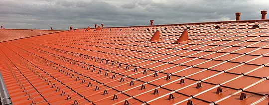 Zdjęcie z bliska dachu PREFA z aluminium o wyglądzie dachówki ceramicznej – dachówka klasyczna PREFA w kolorze ceglastym z barierami śniegowymi
