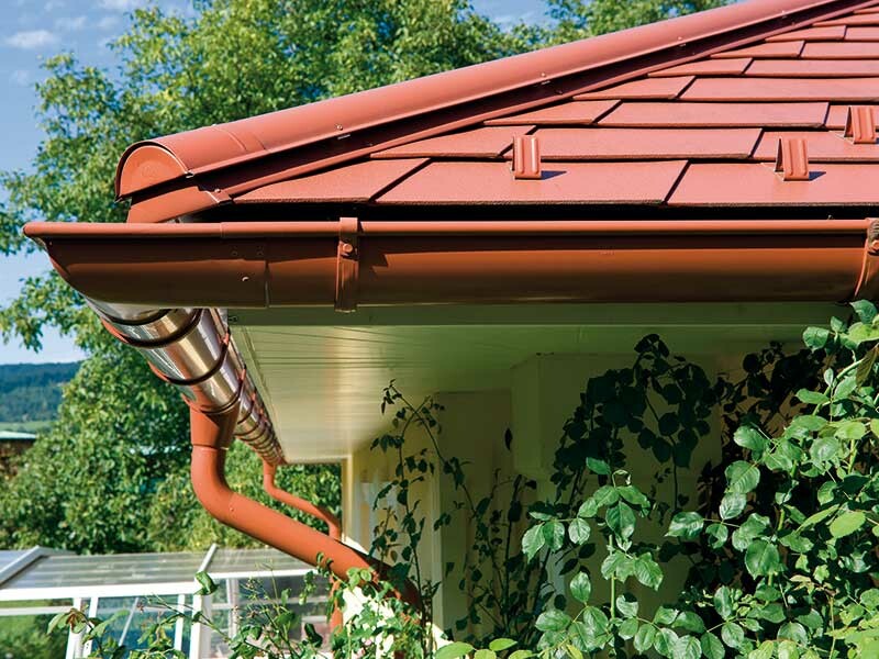 Zdjęcie szczegółowe dachówki łupkowej PREFA w kolorze ceglastym z pasującą do niej rynną dachową także w kolorze ceglastym.