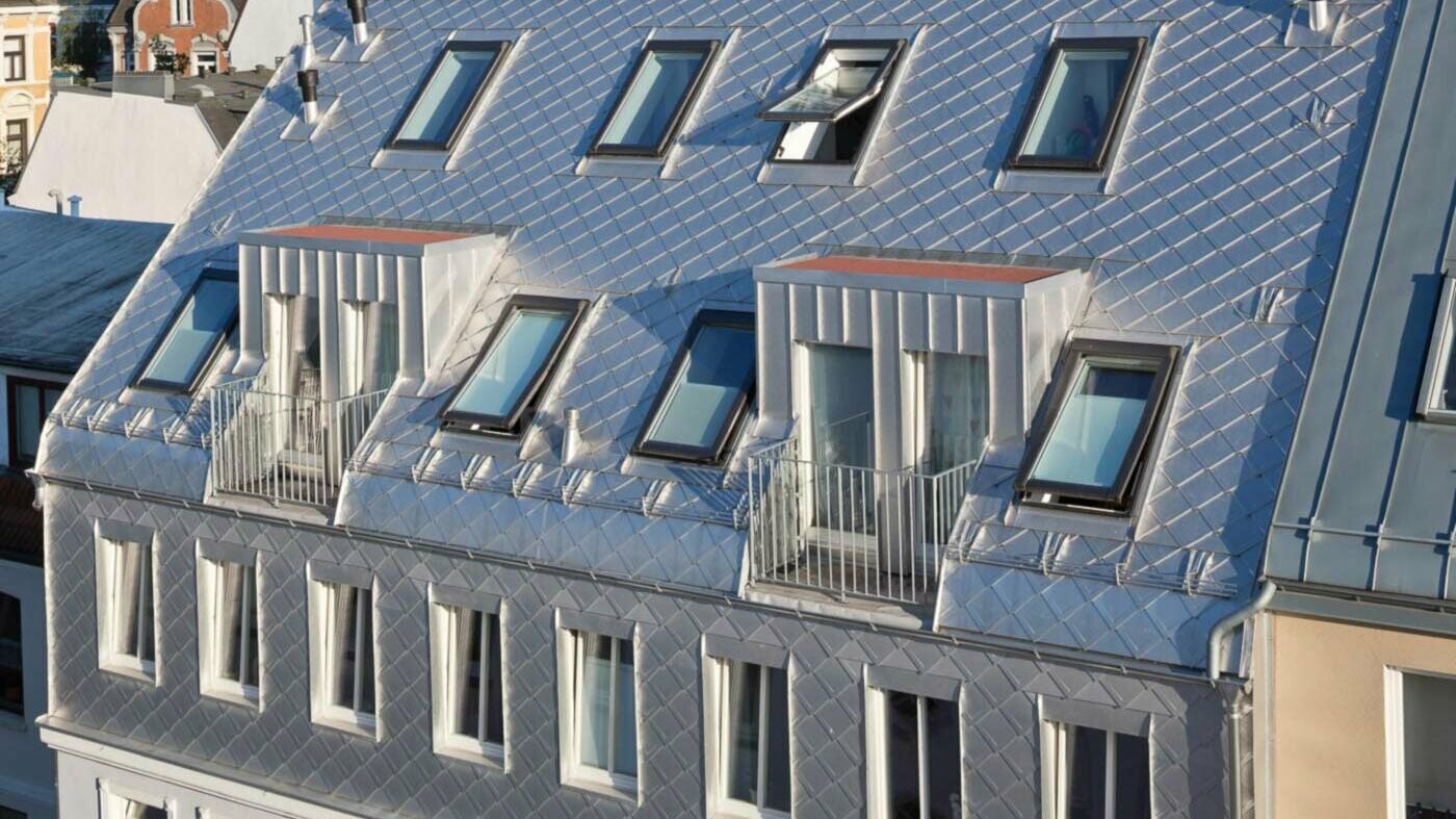 Dach imitujący łuski z niepowlekanego aluminium przy rozbudowie poddasza z wieloma oknami dachowymi