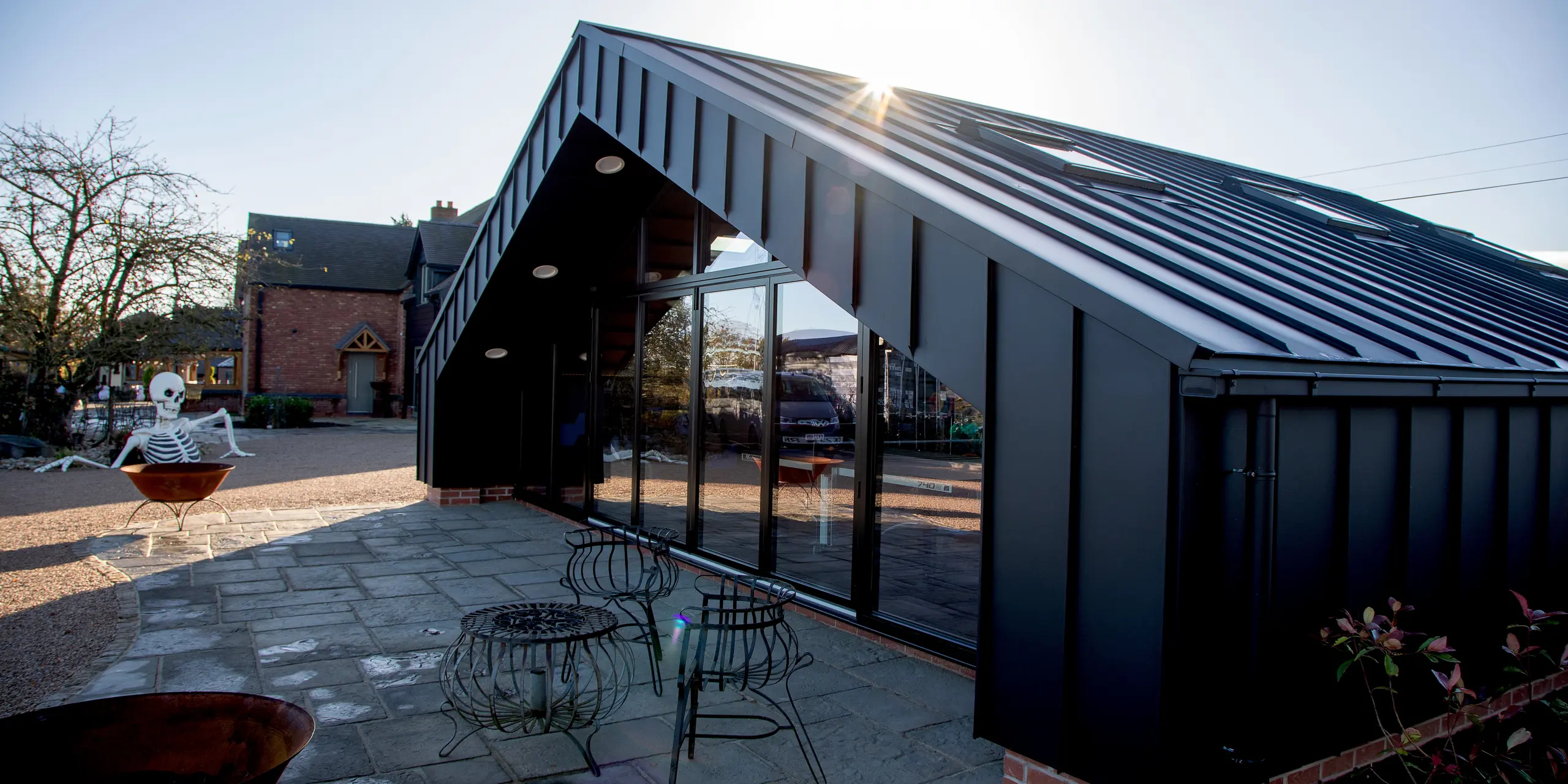 Architektonische Außenansicht des modernen Freizeitgebäudes mit vollständig mit PREFALZ in P.10 Schwarz verkleideter PREFA Aluminiumhülle. Die präzisen Stehfalzlinien, die großzügige Glasfront und die kantige Dachform erzeugen ein dynamisches, hochwertiges Erscheinungsbild. Die robuste, witterungsbeständige Aluminiumoberfläche sorgt für maximale Langlebigkeit und setzt klare architektonische Akzente im Außenbereich.