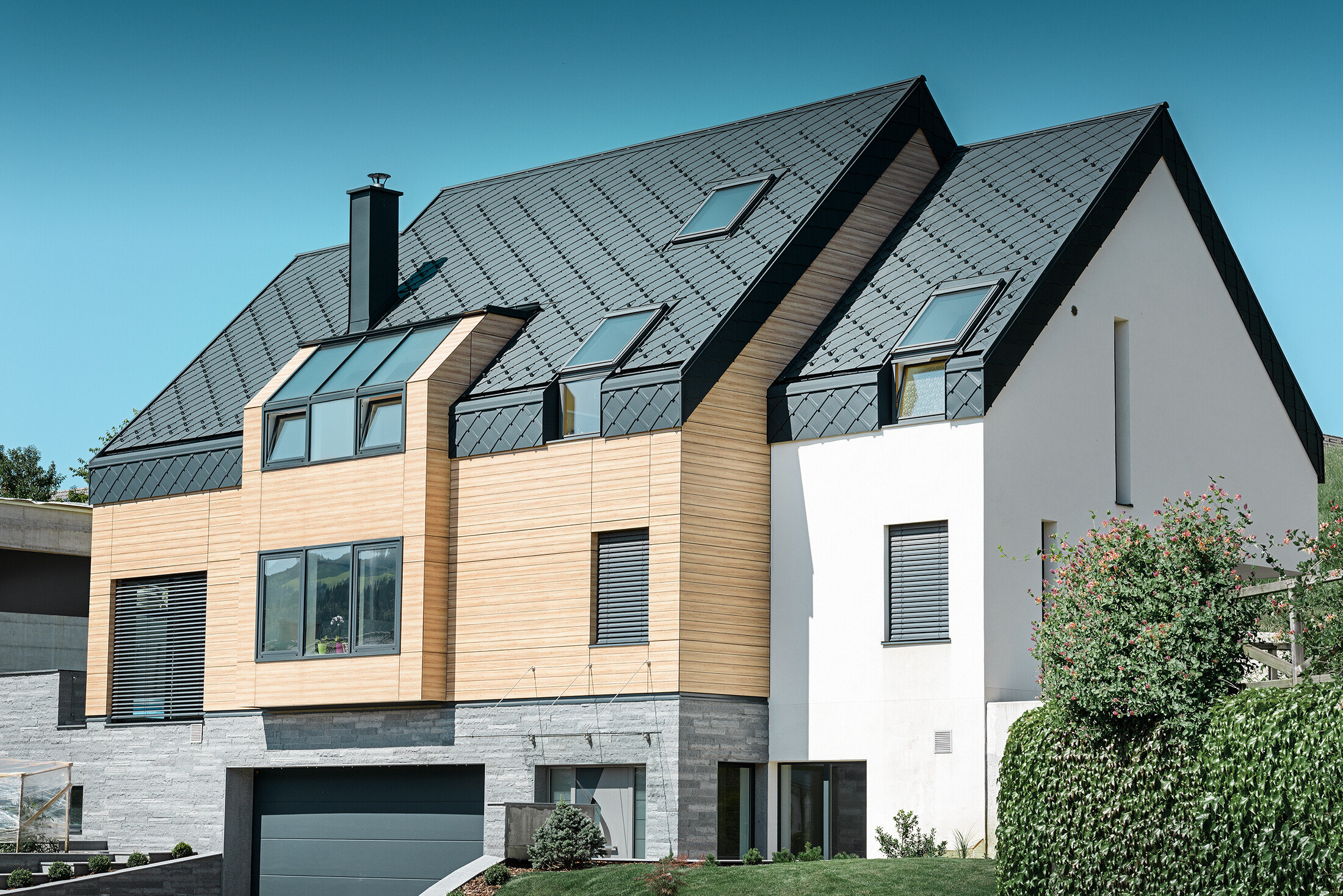 Nowoczesne budownictwo, w którym okładzina dachowa znajduje się również na górnej części elewacji, jako pokrycie dachowe zastosowano aluminiową dachówkę romb w kolorze antracytowym