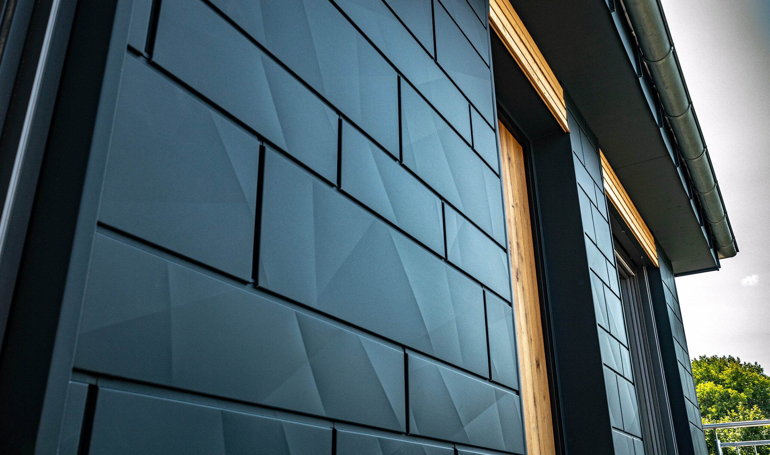 Elewacja z PREFA Siding.X w kolorze antracytowym z drzwiami balkonowymi i dużymi powierzchniami przeszklonymi w połączeniu z drewnianą elewacją.