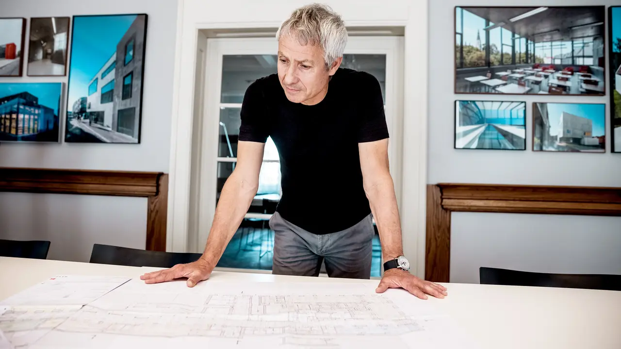 Architekt pracuje nad szczegółowymi planami budowlanymi w nowoczesnym biurze, otoczony imponującymi zdjęciami projektów architektonicznych PREFA.