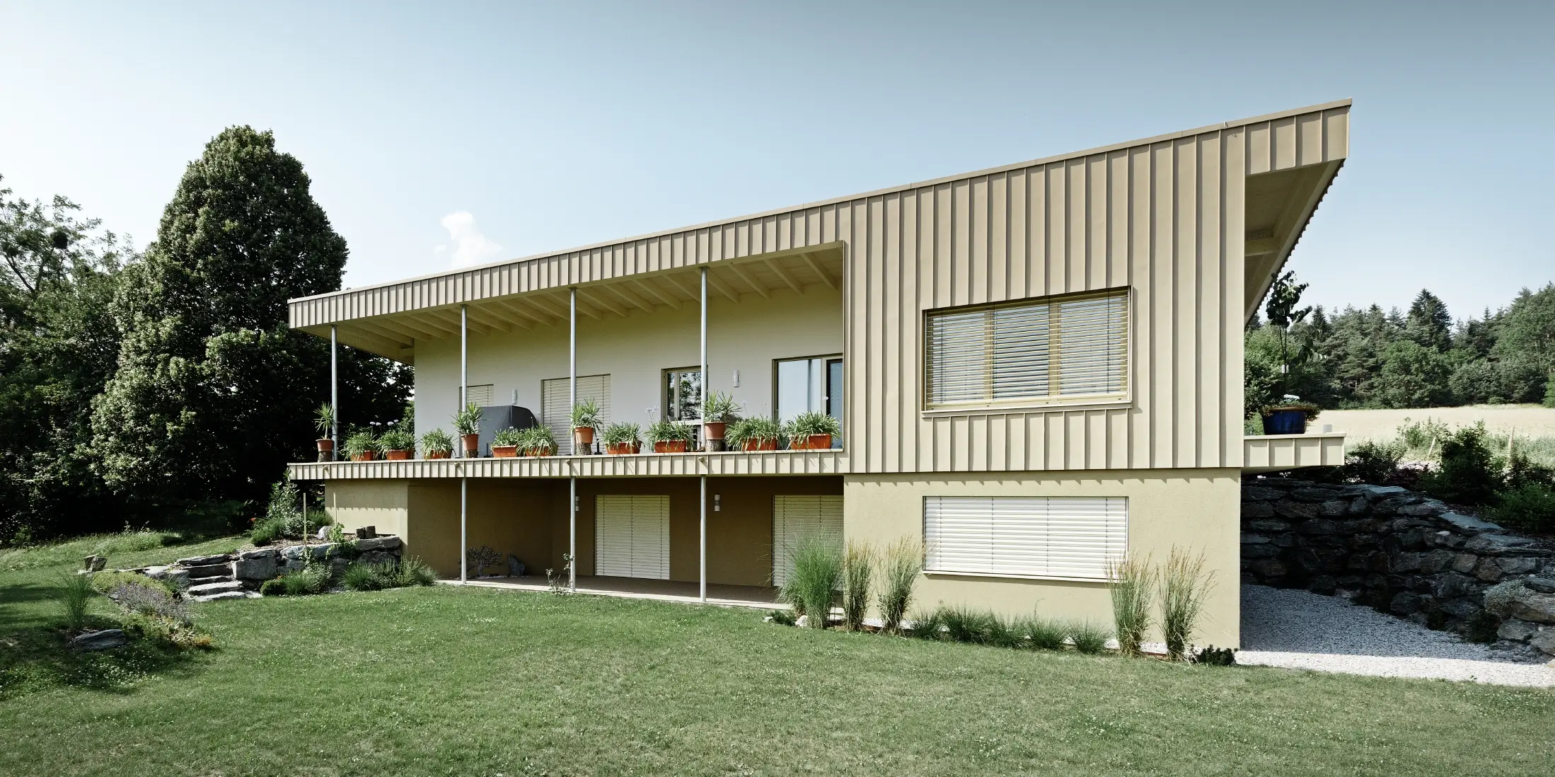 Modernes Einfamilienhaus in Schiefling am See mit großzügiger Terrasse und eleganter PREFALZ Aluminiumfassade in P.10 Sandbraun. Die klaren vertikalen Linien der Gebäudehülle setzen einen markanten architektonischen Akzent und harmonieren mit der natürlichen Umgebung. Die langlebige, wartungsarme PREFA Aluminiumfassade überzeugt durch zeitlose Ästhetik, Widerstandsfähigkeit und hochwertige Verarbeitung.