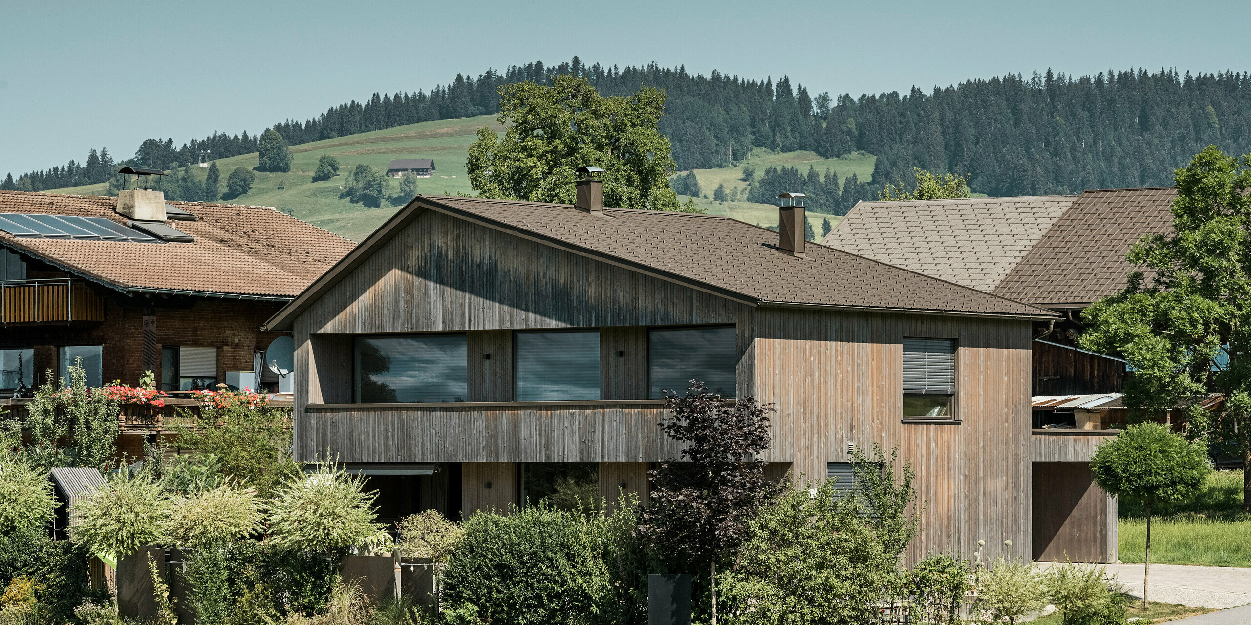 Einfamilienhaus in Krumbach, das sich mit seiner naturbelassenen Holzfassade und dem hochwertigen PREFA Dach in P.10 Braun in die idyllische Landschaft einbettet. Die verwendeten Materialien betonen die ökologische Bauweise des Hauses und die Langlebigkeit des PREFA Dachsystems aus Aluminium. Die PREFA Dachplatten bieten einen dauerhaften und witterungsbeständigen Schutz. Zudem vereint die bewährte Dachplatte Ästhetik und Funktionalität in einem ländlichen Kontext.