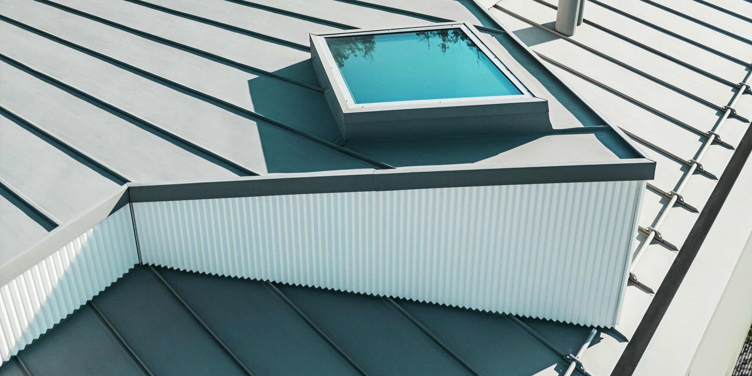 Detailreiche Aufnahme eines PREFALZ Dachs in Patinagrau mit integriertem Oberlicht und vertikalem Zackenprofil am Dachaufbau. Die hochwertige PREFA Stehfalzdeckung bietet optimale Witterungsbeständigkeit und architektonische Präzision. In Kombination mit den klaren Linien der Zackenprofil-Fassade entsteht ein modernes, langlebiges und funktionales Dachsystem.