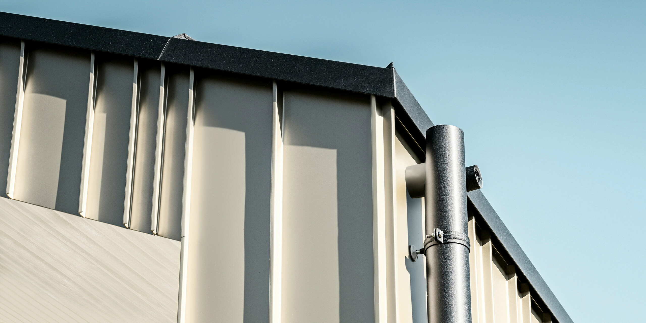 Detailansicht eines robusten PREFA Dachentwässerungssystems aus Aluminium. Das anthrazitfarbene Ablaufrohr bietet eine langlebige und wartungsarme Lösung für moderne Architektur. Die präzise Verarbeitung und das elegante Design unterstreichen die Qualität von PREFA Aluminiumprodukten, die sowohl funktional als auch ästhetisch ansprechend sind und zur Wertsteigerung des Objekts beitragen. Angebracht wurde das Dachentwässerungssystem auf einem modernen Neubau in Bad Münstereifel. Das Einfamilienhaus verfügt über eine elegante Fassade aus FALZONAL in der Farbe Lichtbronze. 