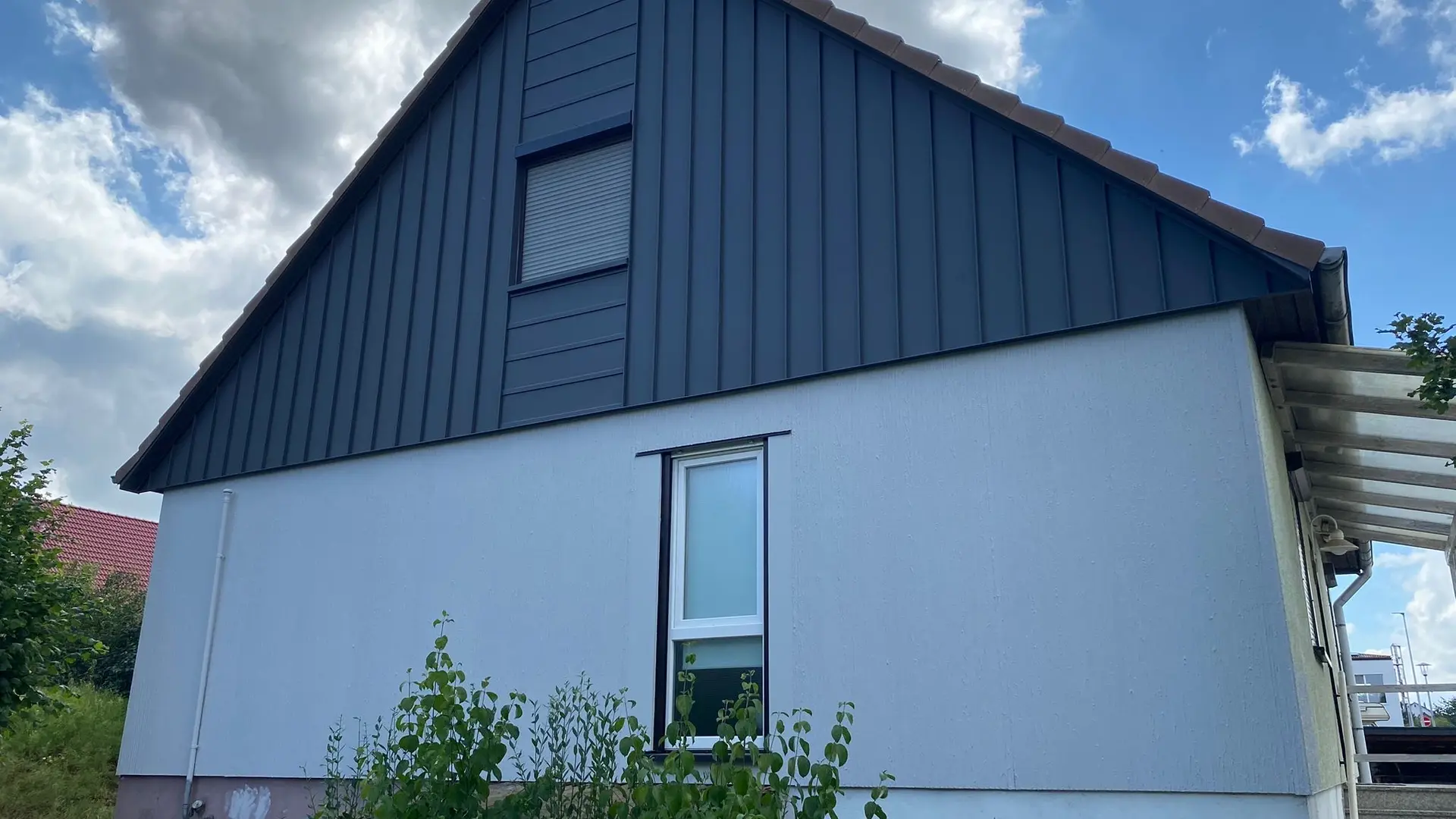 Ein Einfamilienhaus nach der Sanierung mit einer modernen Aluminiumfassade von PREFA. Die robuste Winkelstehfalzfassade in Kombination mit einer abgesetzten Liegefalzfassade in PREFALZ P.10 Dunkelgrau sorgt für eine langlebige, witterungsbeständige Ausführung und verleiht dem Gebäude eine zeitgemäße Optik.