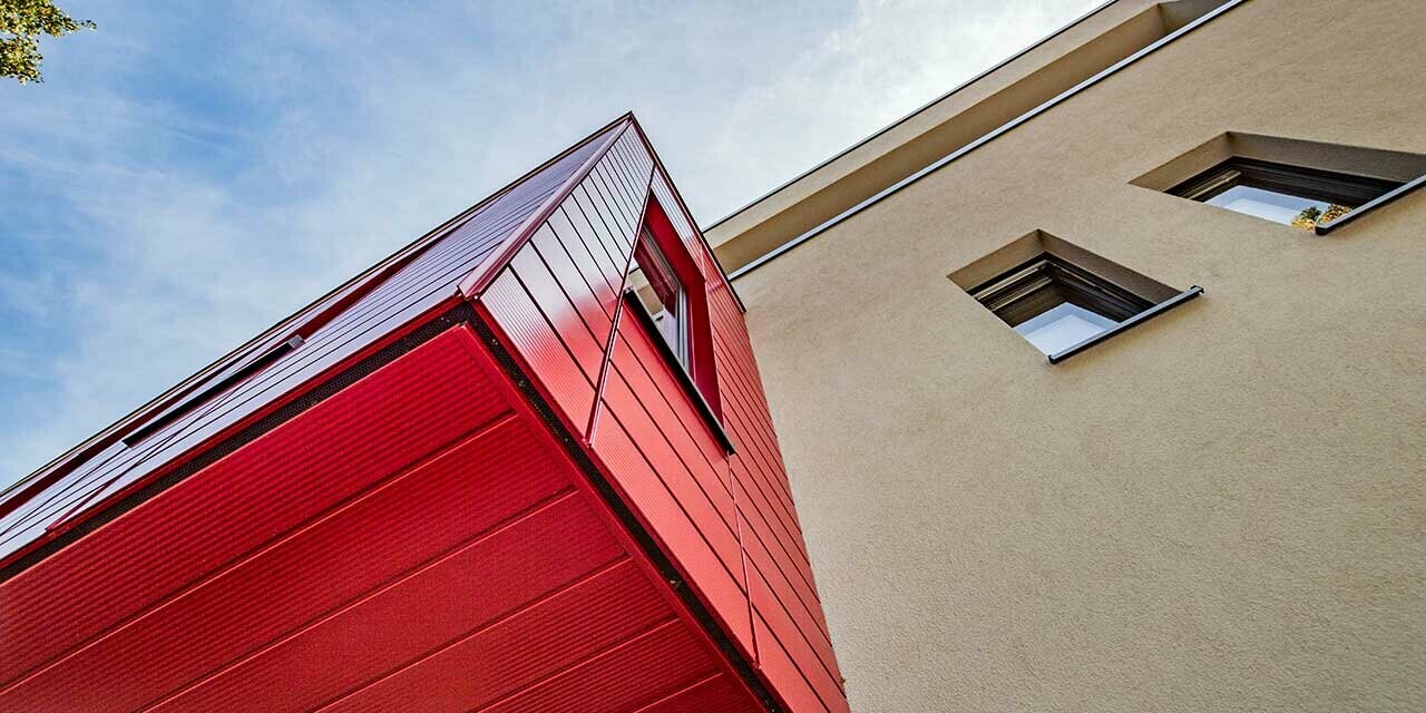 Wykusz z rubinowymi sidingami PREFA w linie na nowoczesnym domu jednorodzinnym w Wernigerode. Tutaj sfotografowano od dołu wystającą dobudówkę.