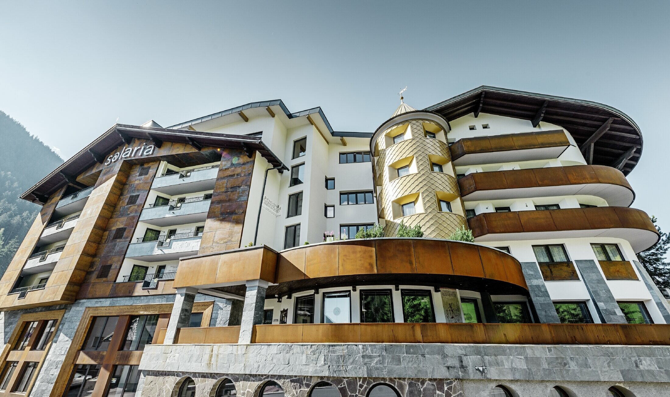 Tradycyjny hotel w Ischgl z drewnianymi balkonami i drewnianą elewacją oraz wieżą pokrytą złotymi rombami aluminiowymi PREFA