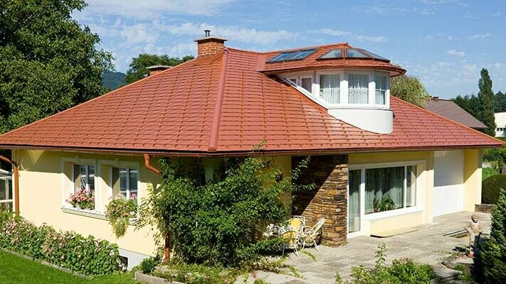 Dom jednorodzinny z dachem czterospadowym i lukarną, kryty gontem aluminiowym PREFA w kolorze czerwonej cegły.