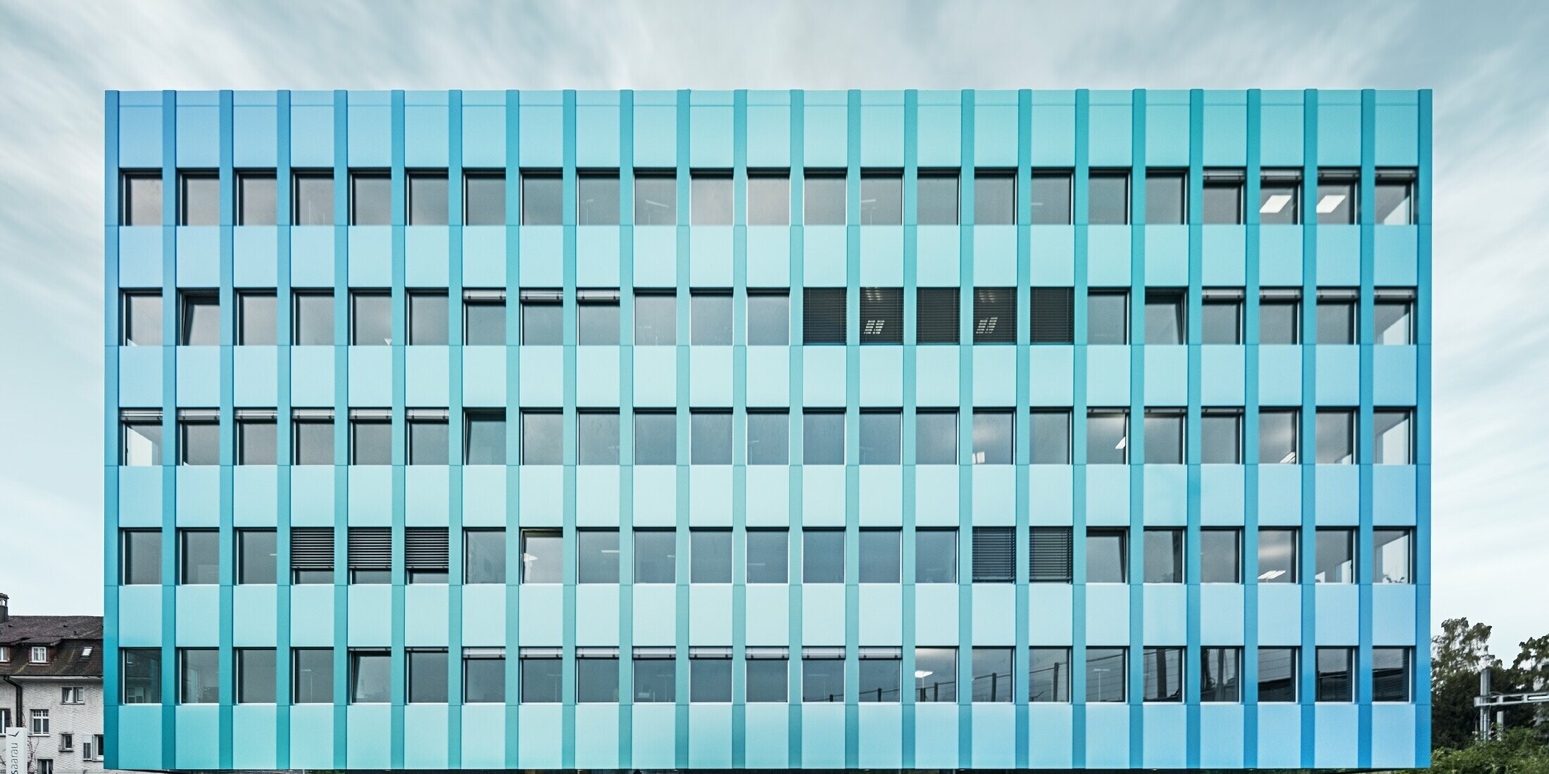 Frontale Ansicht des Wielandhauses in Aarau mit vielen Fenstern und einer blau-grünen PREFABOND Aluminiuim Verbundplatten-Fassade von PREFA. Die Fassade schimmert in blau/grün durch das eigene Beschichtungsverfahren.