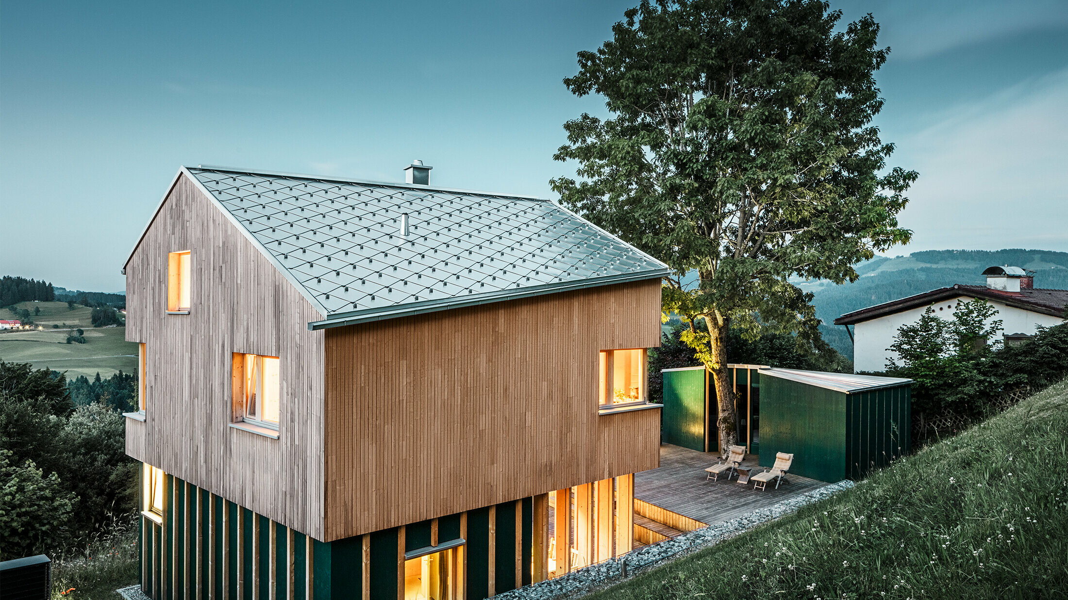 Nowo wybudowany dom jednorodzinny z drewnianą elewacją i naturalnym dachem PREFA z elementów w kształcie rombu