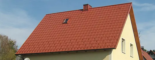 Klasyczny dach dwuspadowy z małym oknem dachowym i kominem, pokryty dachówką klasyczną PREFA w kolorze ceglastym wraz z barierami śniegowymi i zabezpieczającymi hakami dachowymi.