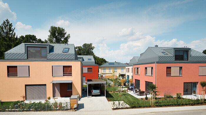Osiedle domów wielorodzinnych z elewacjami w odcieniach czerwieni i aluminiowymi dachami rombowymi w kolorze jasnoszarym marki PREFA
