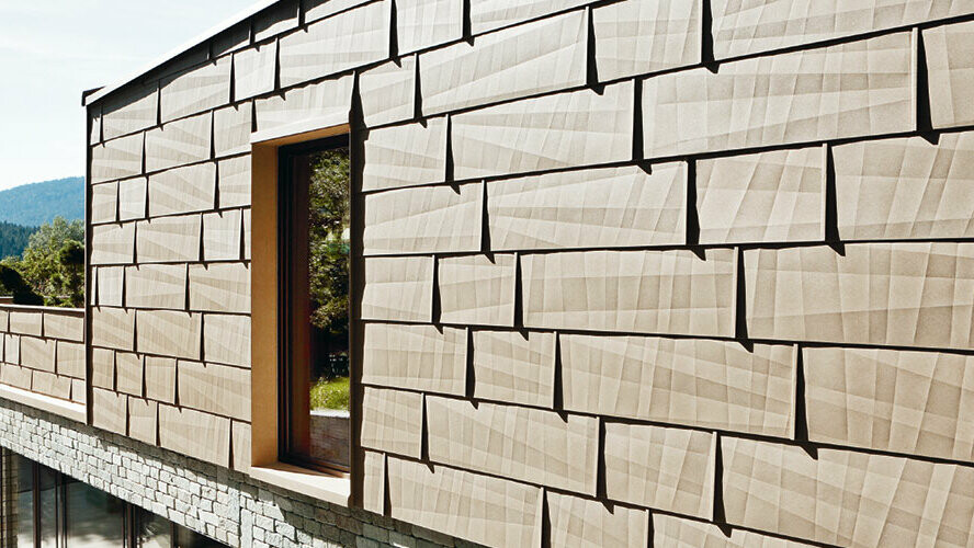 Ta fasada zewnętrzna stanowi połączenie paneli elewacyjnych PREFA FX.12 w kolorze P.10 brąz piaskowy z kamienną fasadą piwnicy.