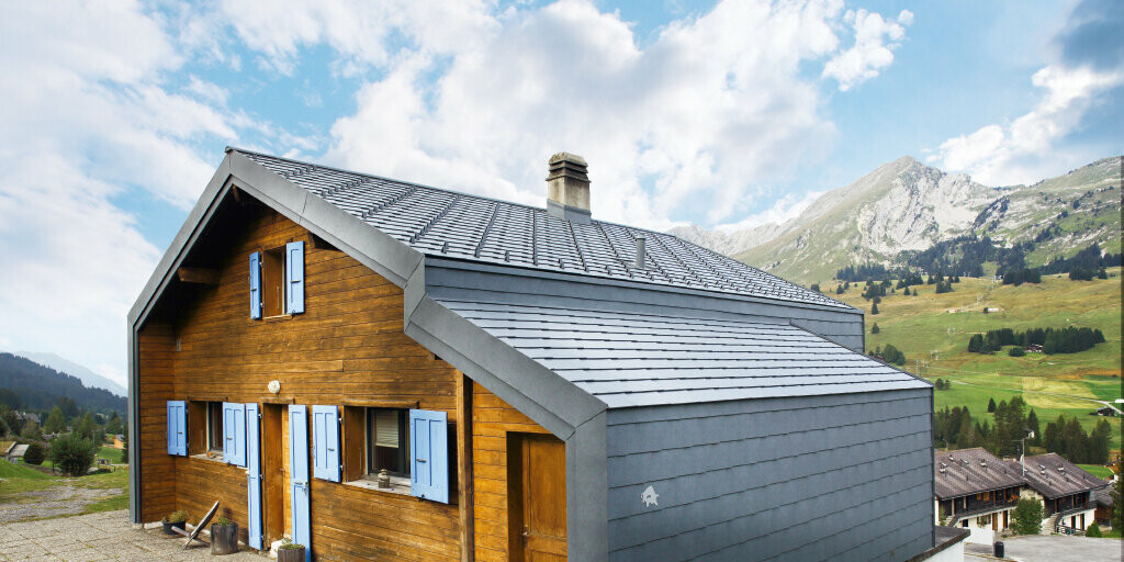 Dom w górach Szwajcarii z elewacją drewnianą w połączeniu z dachem PREFA oraz rombem elewacyjnym w kolorze szary kamienny