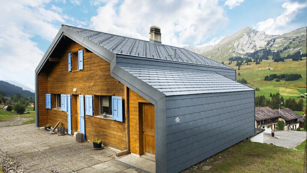 Dom w górach Szwajcarii z elewacją drewnianą w połączeniu z dachem PREFA oraz rombem elewacyjnym w kolorze szary kamienny