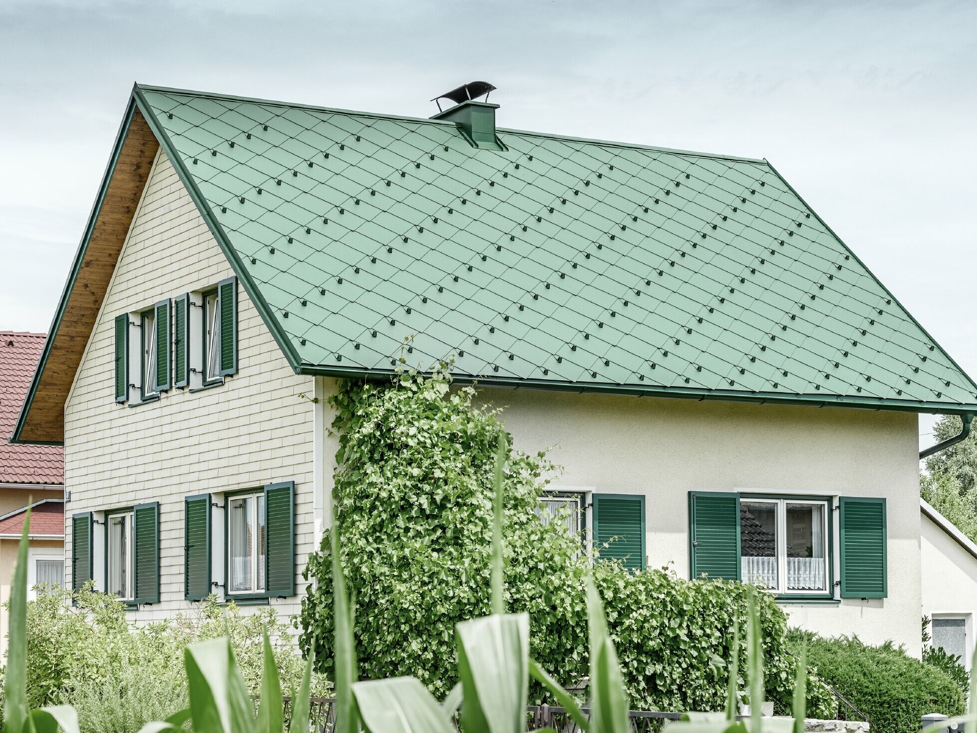 Klasyczny dom jednorodzinny z dachem dwuspadowym, pokryty aluminium w kolorze zielenimchu z zielonymi okiennicami
