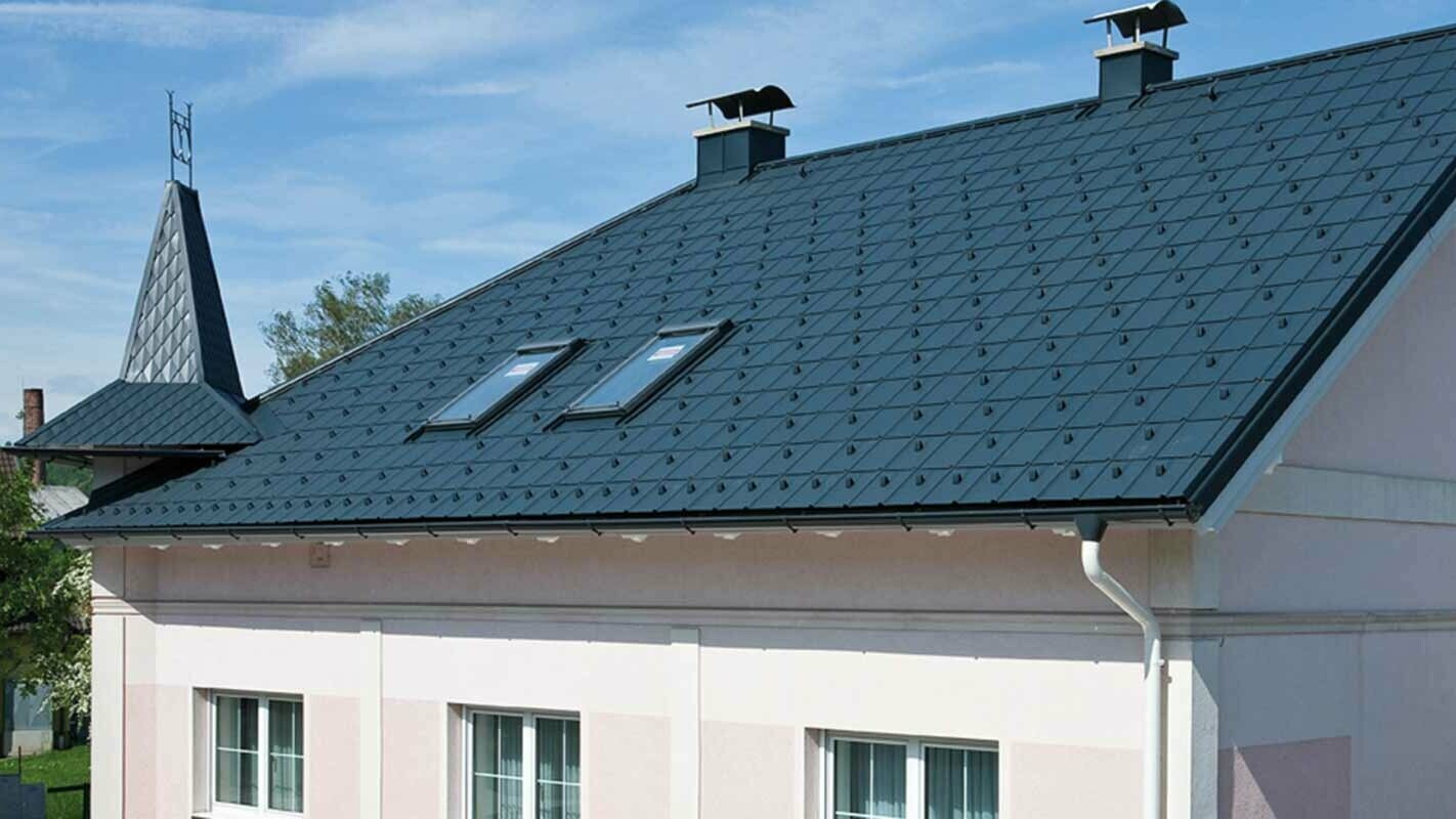 Dom po modernizacji dachu z płytą dachową PREFA w Austrii — wcześniej cement włóknisty, eternit, z wieżyczkami i czerwoną elewacją