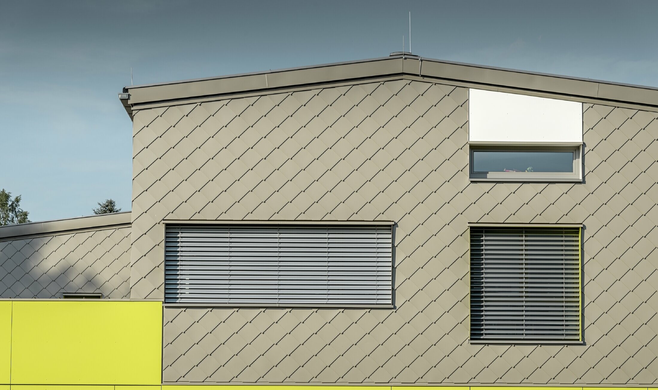 Widok detalu elewacji z rombem fasadowym PREFA 29 × 29 w kolorze brązowym z trzema oknami bez okapu. 