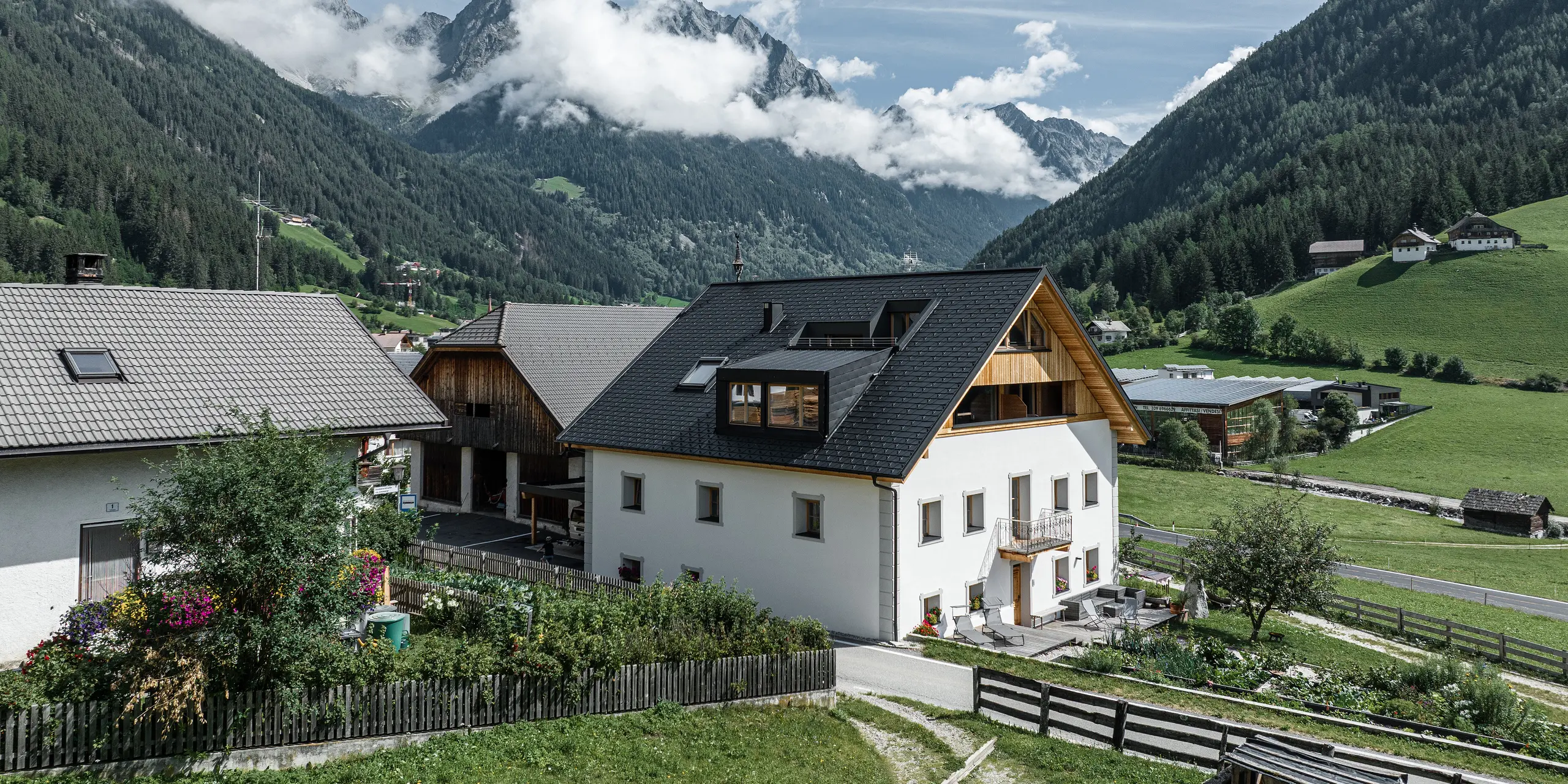 Blick auf die Ferienwohnungen Ausserwegerhof im Antholzertal, Südtirol, vor einer beeindruckenden Bergkulisse. Das Gebäude zeichnet sich durch ein PREFA Dach mit anthrazitfarbenen DS.19 Dachschindeln aus. Das Aluminium-Satteldach fügt sich harmonisch in die umliegende Landschaft ein.