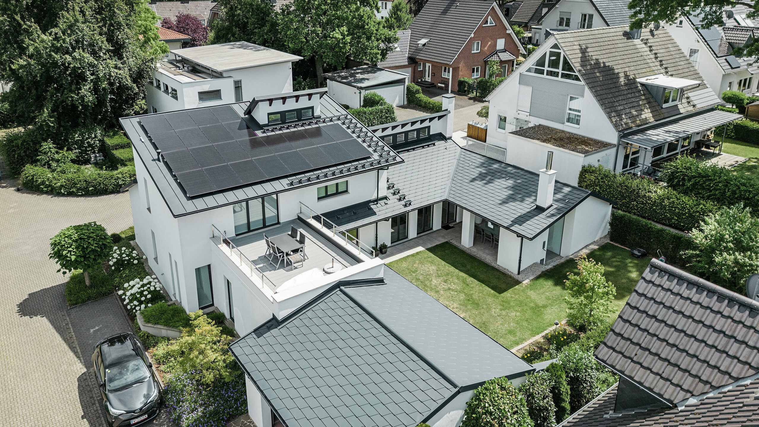 Widok z lotu ptaka na wyjątkowy krajobraz dachu domu jednorodzinnego w Dortmundzie z gontami dachowymi PREFA DS.19 i PREFALZ w kolorze antracytowym P.10 oraz wielkoskalową instalacją fotowoltaiczną.