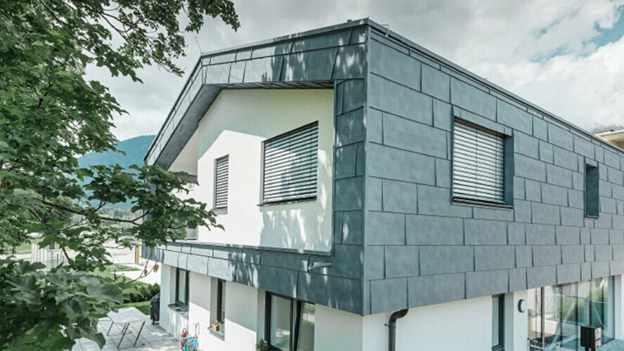 Pierwsze piętro nowoczesnego domu mieszkalnego pokryte aluminiowymi panelami elewacyjnymi PREFA FX.12 w kolorze szarym kamiennym.
