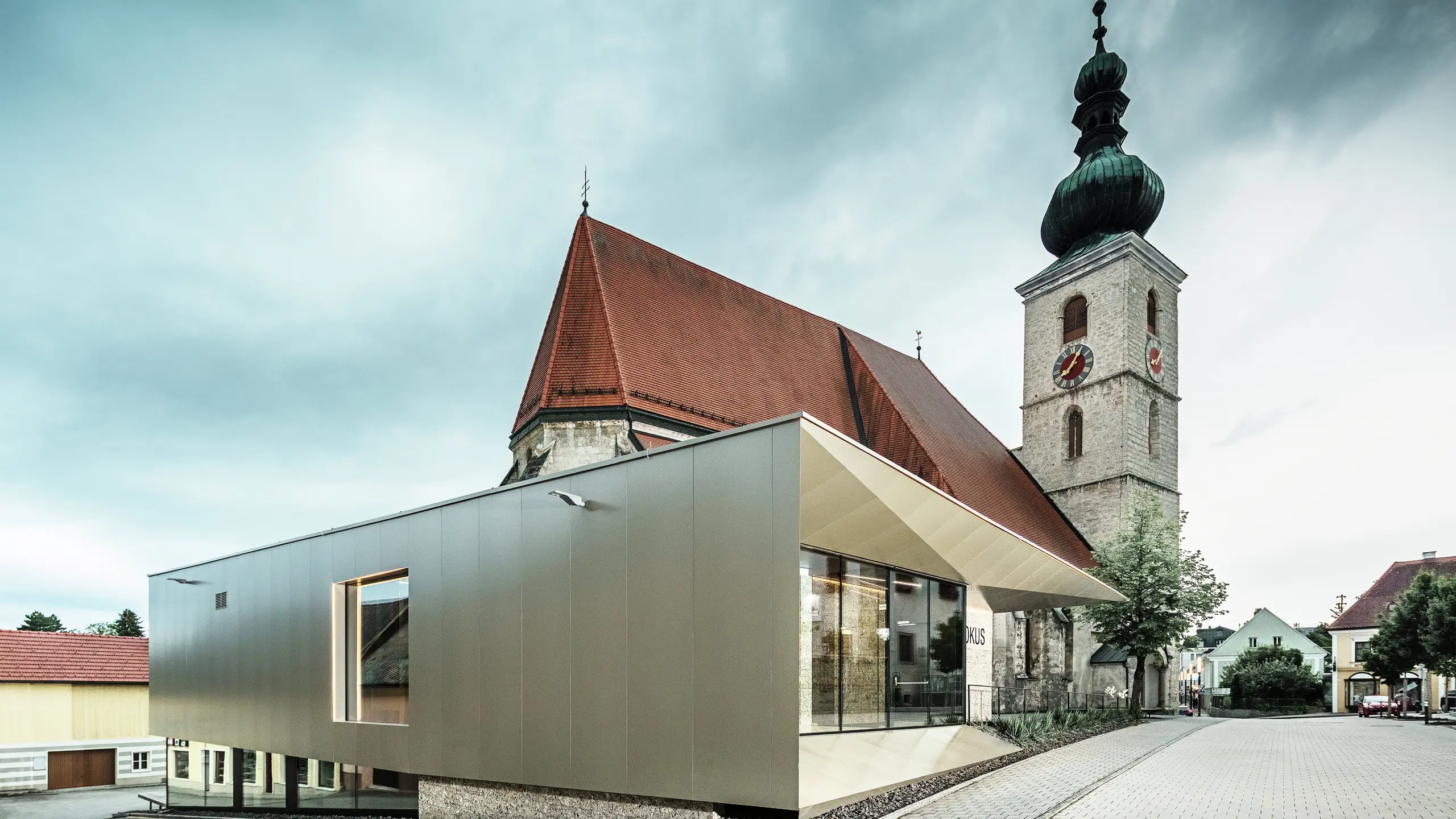 Widok z boku pokazuje filigranowy okap dachowy, wykonany z wysokiej jakości aluminiowych płyt kompozytowych PREFA. Precyzyjne wykończenie nadaje mu nowoczesny wygląd o wyraźnych liniach i podkreśla architektoniczne połączenie starego z nowym.