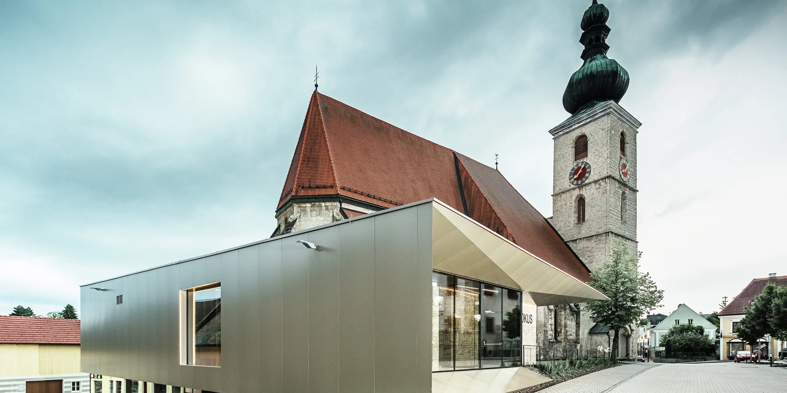 Widok z boku pokazuje filigranowy okap dachowy, wykonany z wysokiej jakości aluminiowych płyt kompozytowych PREFA. Precyzyjne wykończenie nadaje mu nowoczesny wygląd o wyraźnych liniach i podkreśla architektoniczne połączenie starego z nowym.